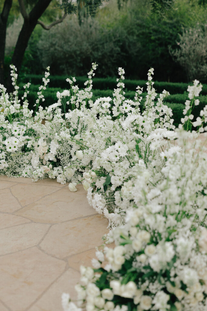 Low floral arc of white flowers and minimal greenery for wedding ceremony.