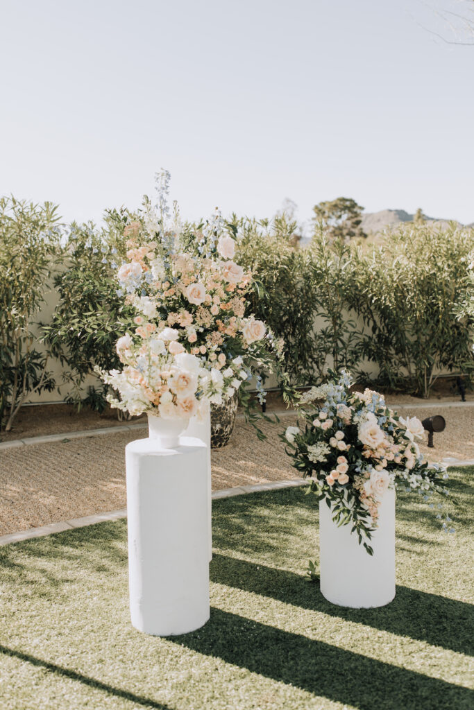 Ceremony altar space wedding flowers placed on round cylinder pillars of white, blush, and blue flowers with greenery.