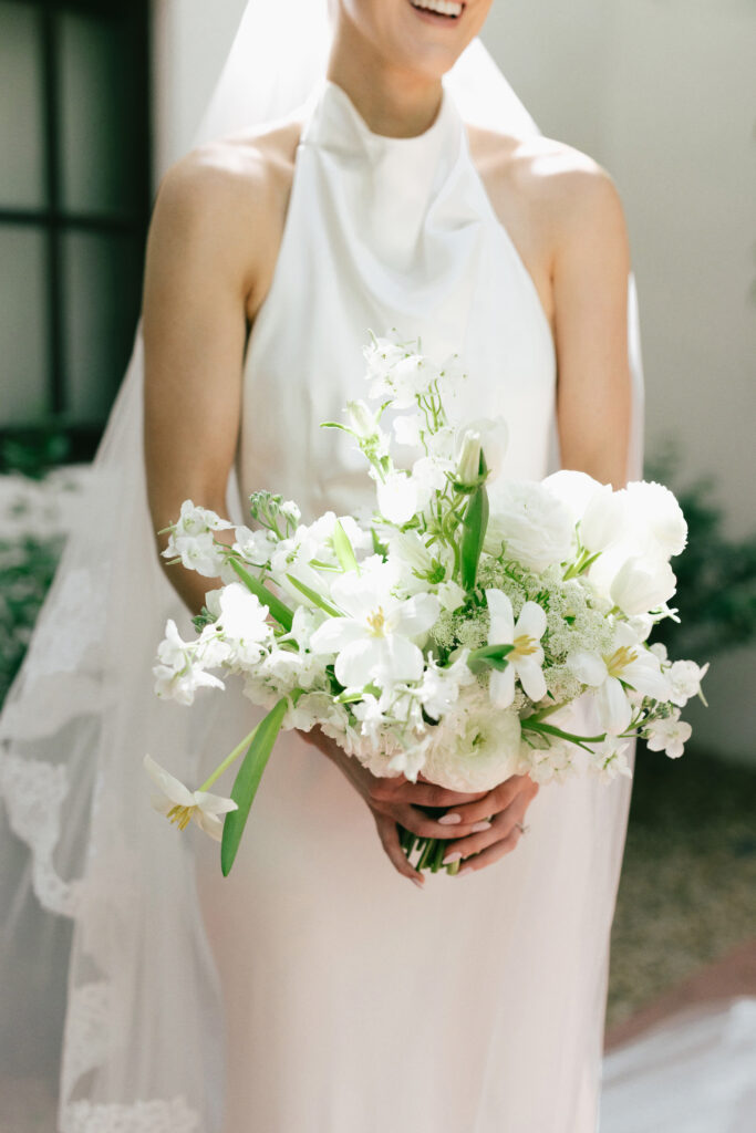 Bride holding bouquet of white flowers with minimal greenery.