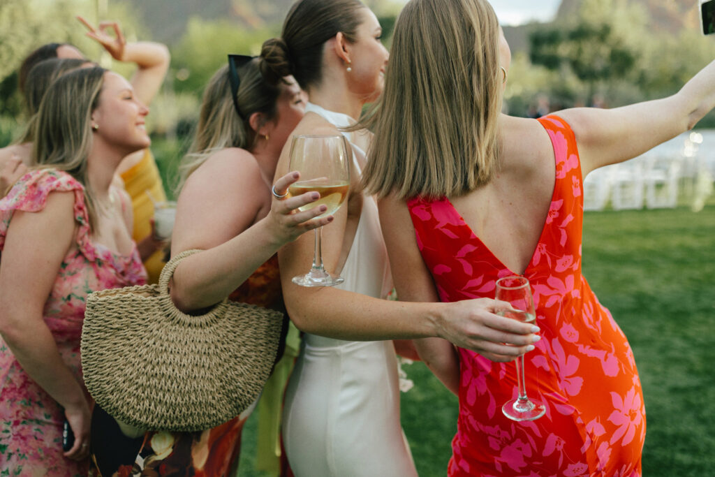 Women dressed semi-formal style holding glasses while taking a selfie outside.