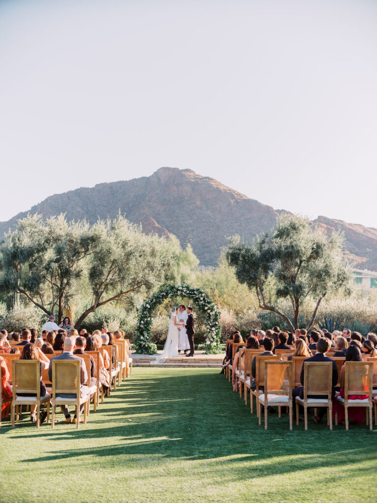 Outdoor ceremony at El Chorro with guests seated and bride and groom in altar space under greenery and floral arch.