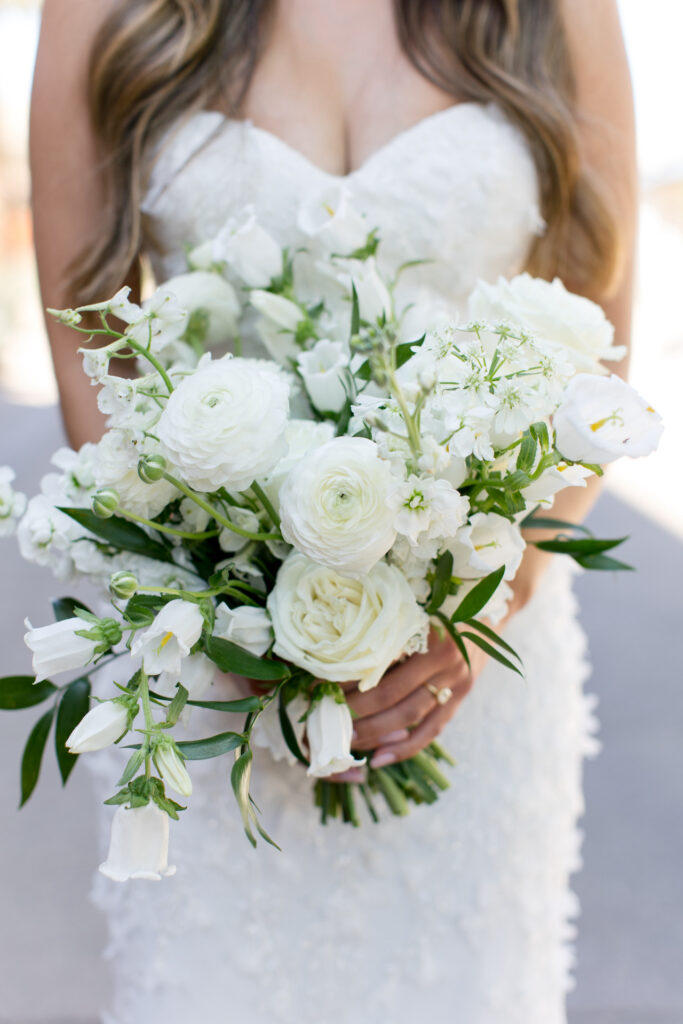 Bride holding bouquet of white flowers and greenery.