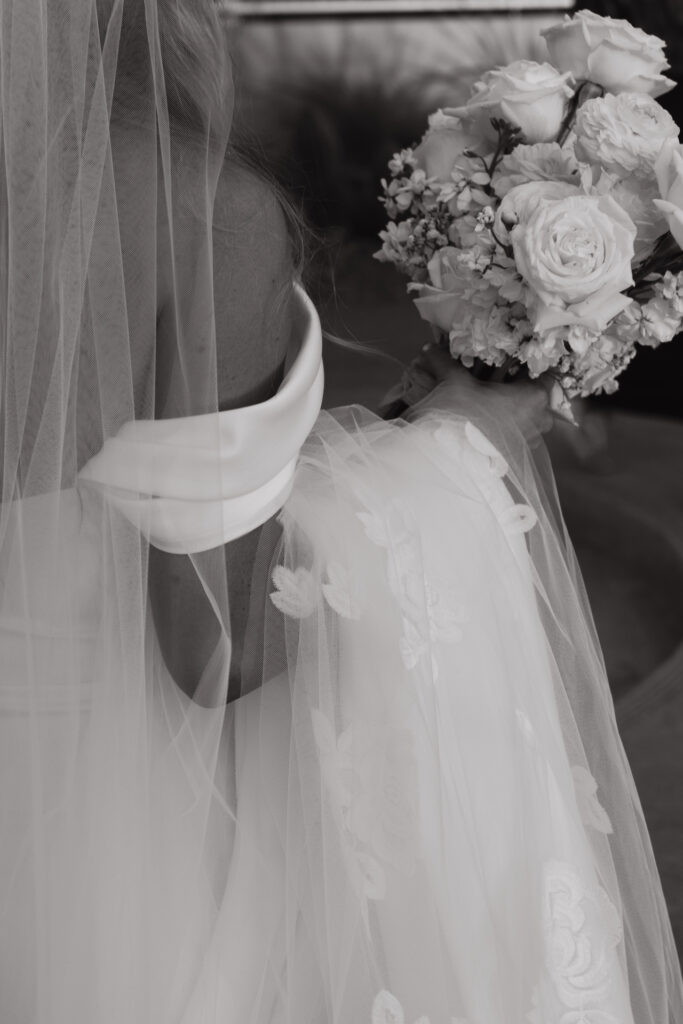 Black and white photograph of bride holding bouquet with her veil hanging over her arm.