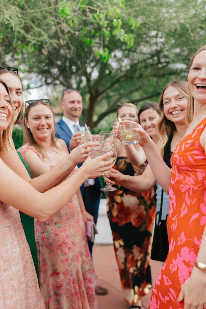 Wedding guests toasting wine and cocktail hour glasses, smiling.