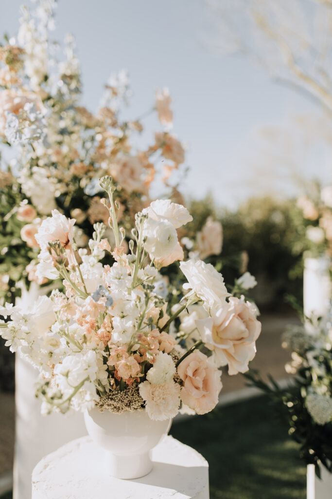 Ceremony altar space wedding flowers placed on round cylinder pillars of white, blush, and blue flowers with greenery.