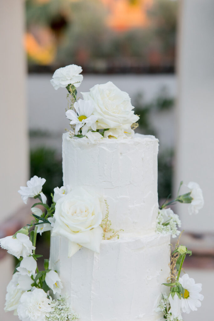 Tiered wedding cake with textured frosting and added white flowers.