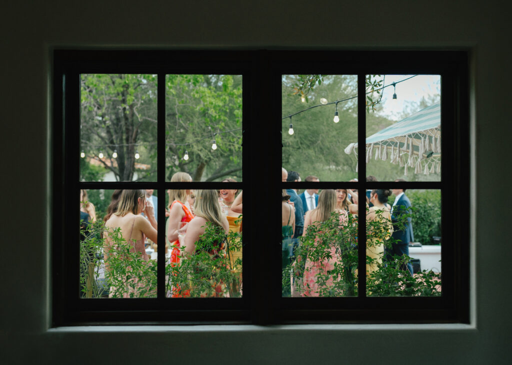 View of wedding guests standing outside through window.