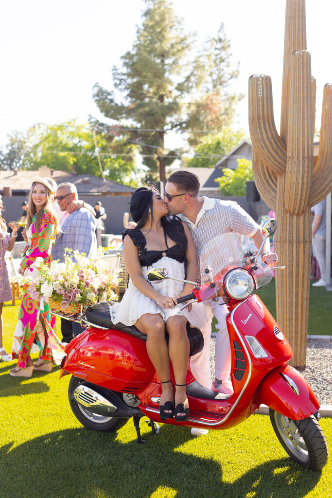 Woman and man kissing while she is seated on red scooter.