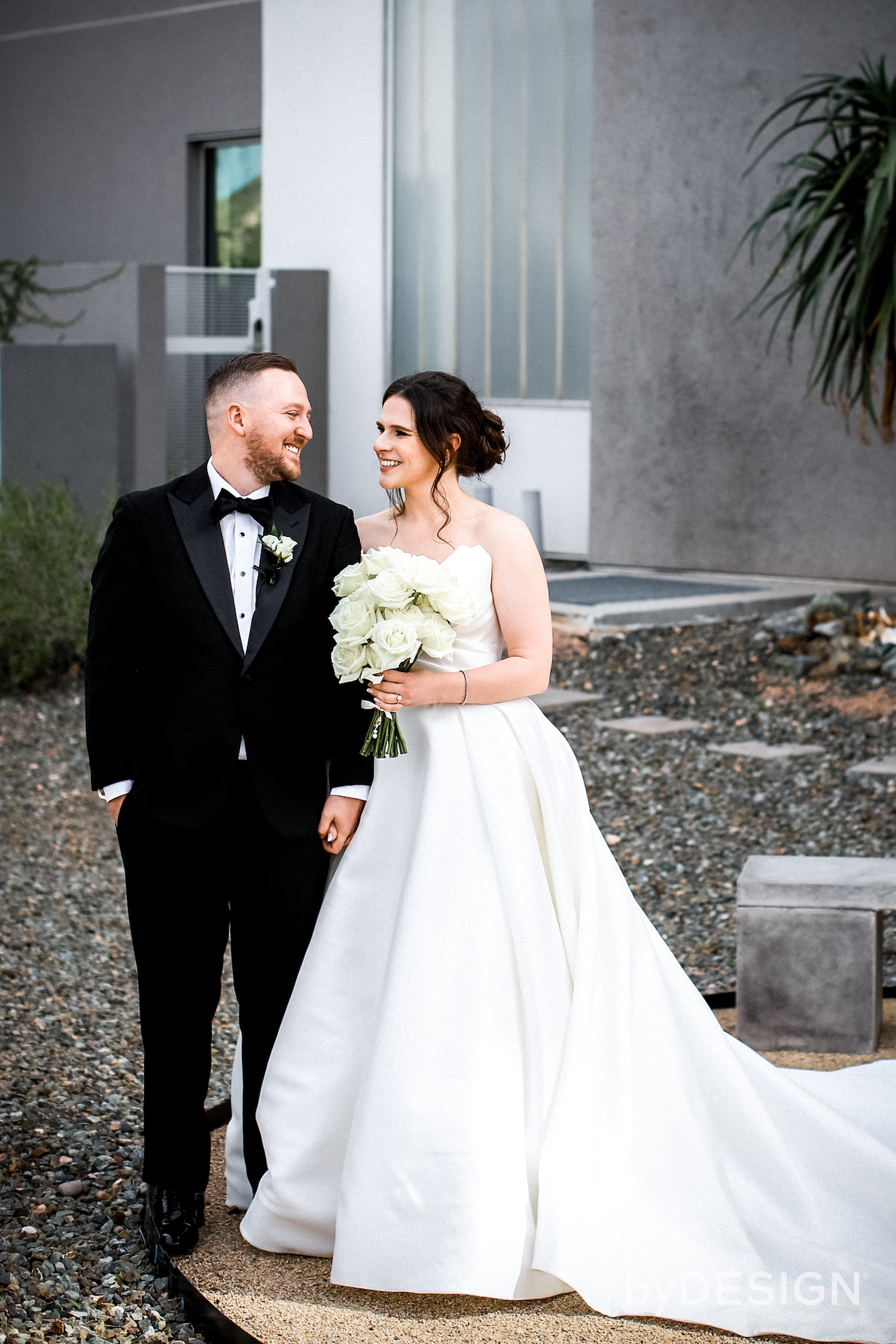 Bride and groom standing closely together in desert landscape area of resort with gravel.