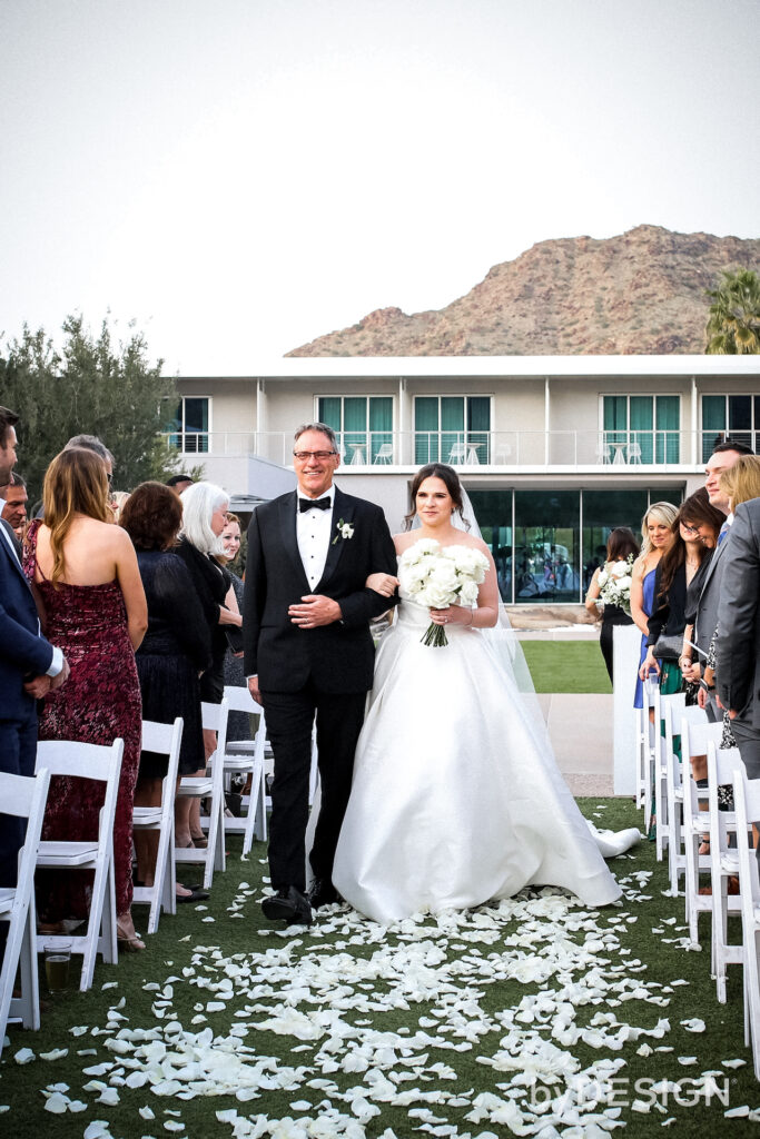 Bride entering ceremony space down aisle covered in white rose petals.