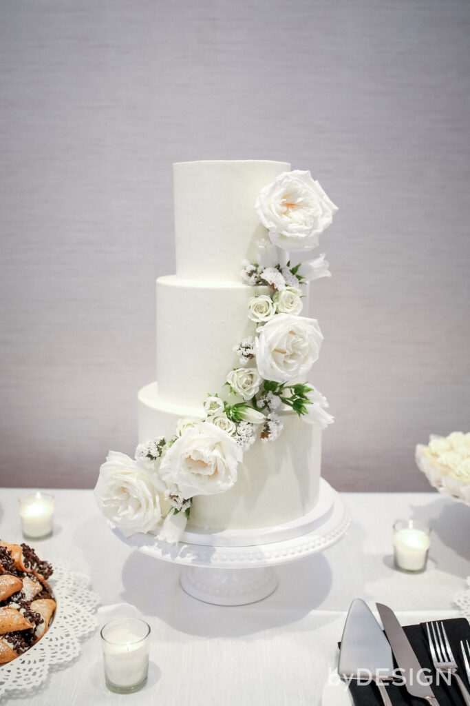 White tiered wedding cake with white flowers added.