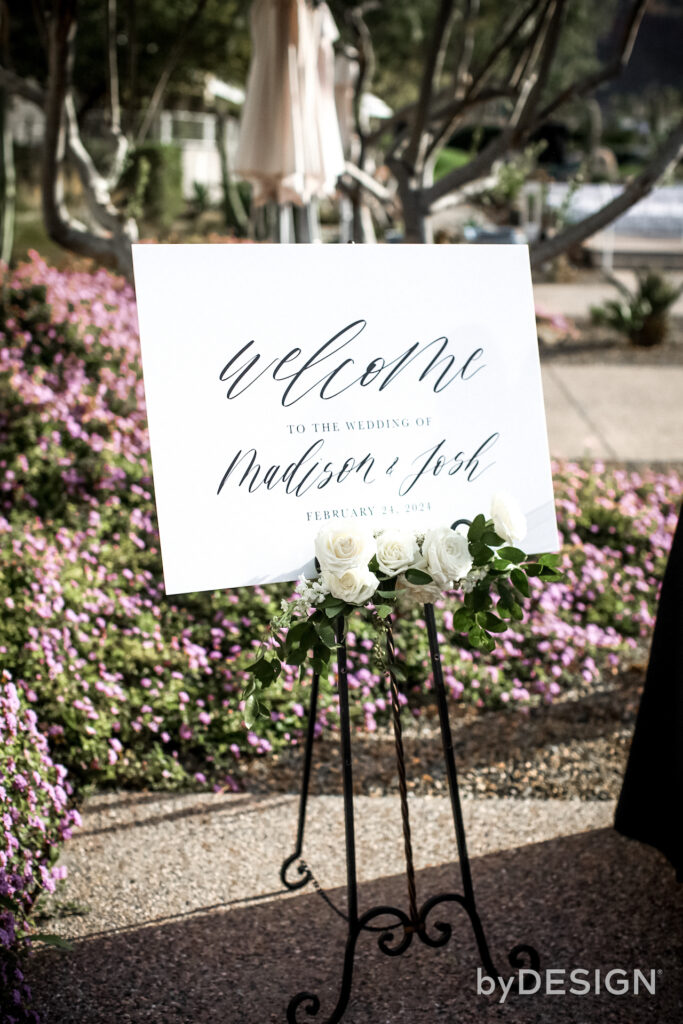 Wedding welcome sign with simple white flower and greenery spray.