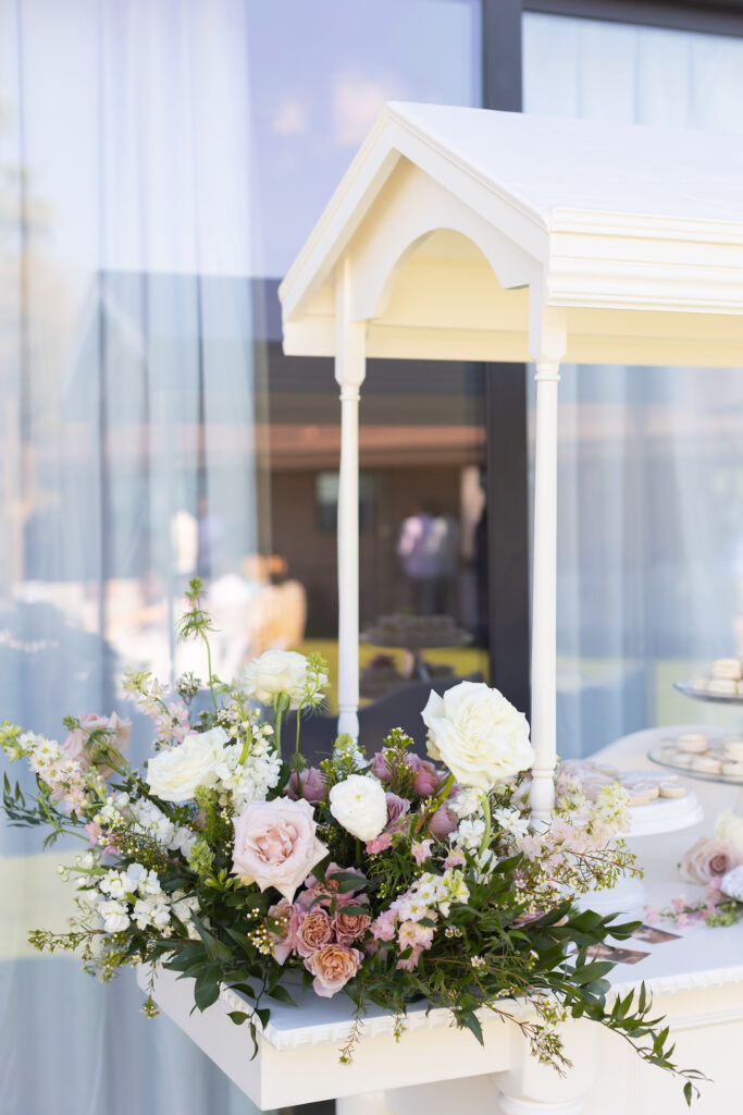 Dessert cart at baby shower with flowers placed on outside ledge of pink and white colors in wooden basket.