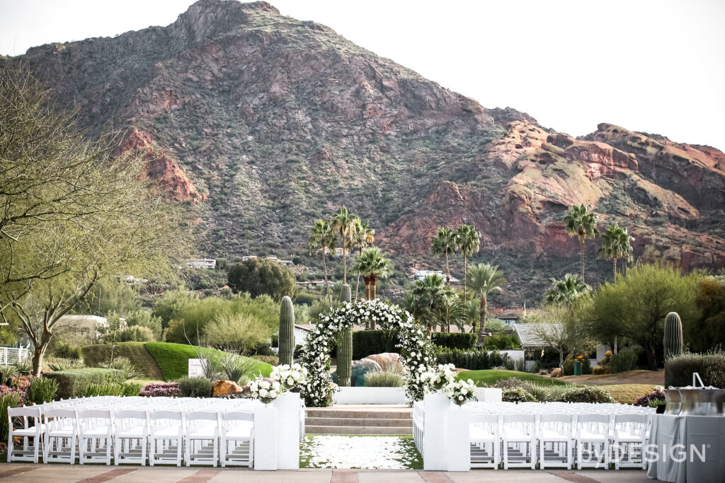 Wedding ceremony space at Mountain Shadows without guests yet. White flower petals down aisle, entrance of the aisle white floral on pillars and front altar space arch.