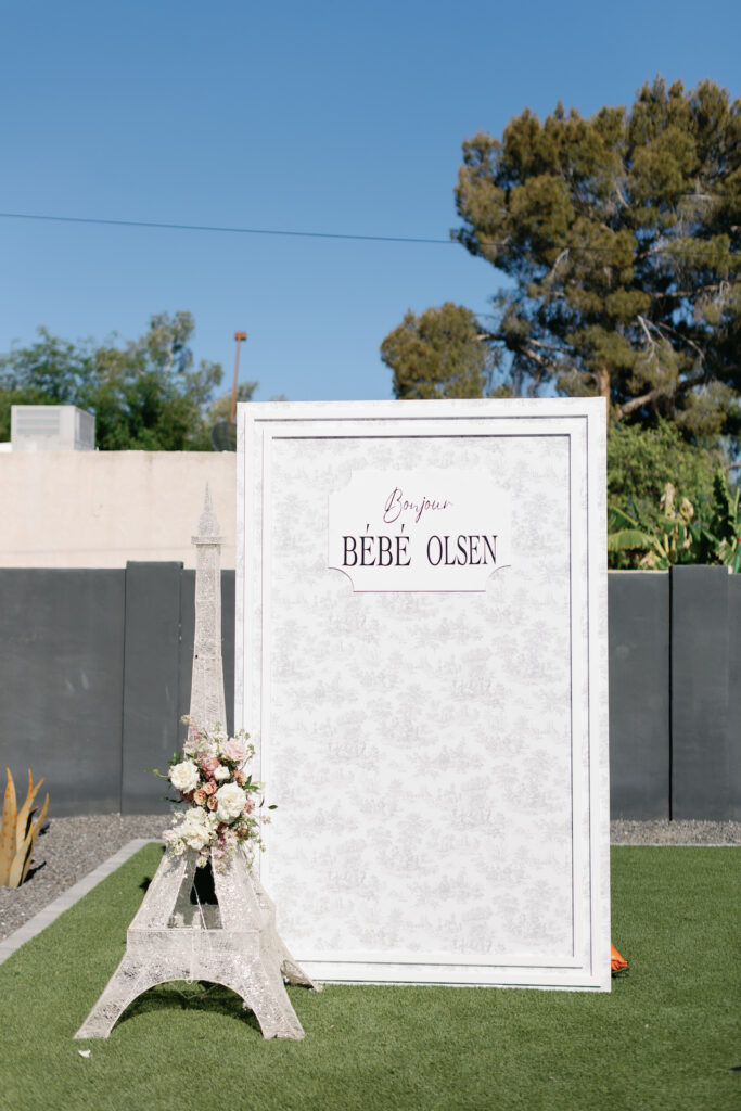 Paris themed baby shower photo backdrop with miniature Eiffel Tower with flowers added to it.