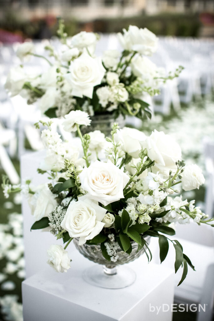 White wedding flowers with greenery in glass vaes on white pillars.