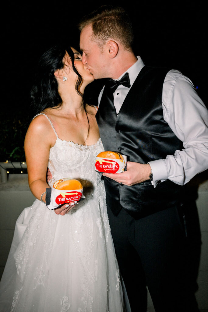 Bride and groom kissing, holding In & Out burgers in custom wrappers with their name on it.