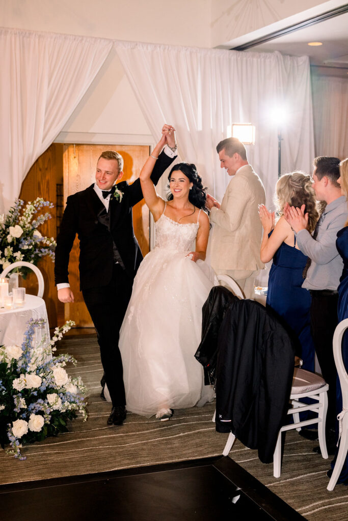 Bride and groom entering reception holding hands up above their heads.