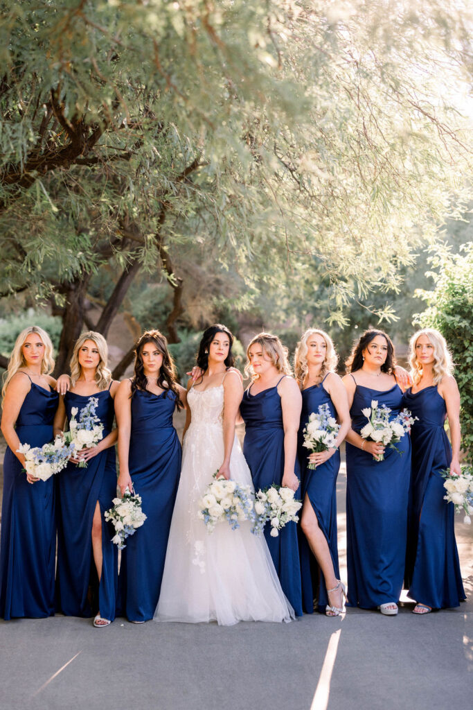 Bride standing in a line with bridesmaids in navy dresses, all holding bouquets.