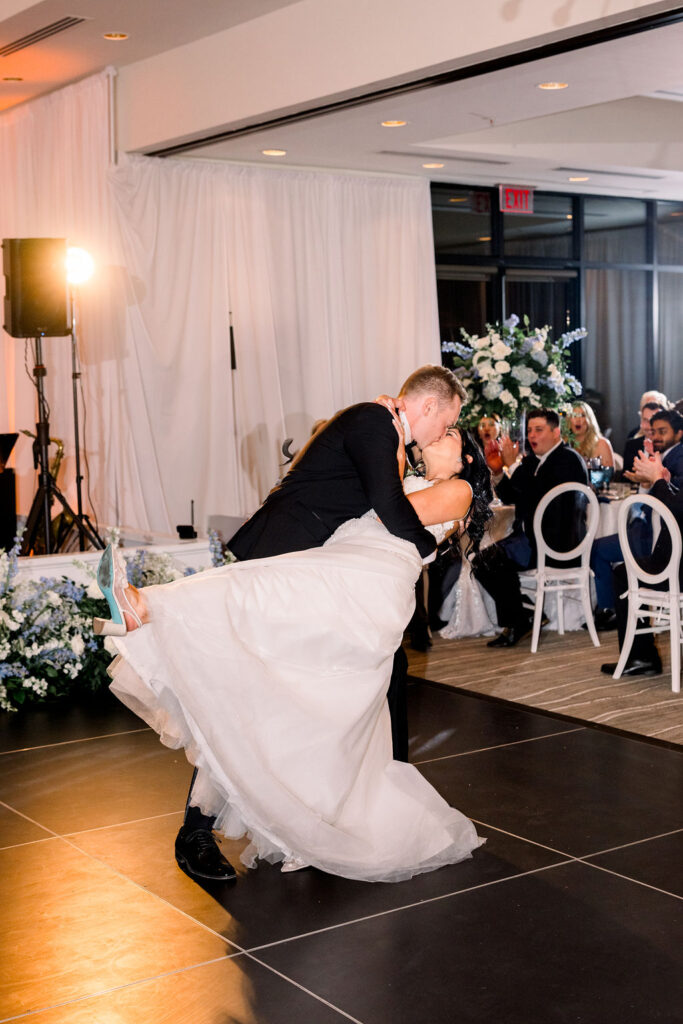 Groom dipping bride and both kissing on dance floor during wedding reception.