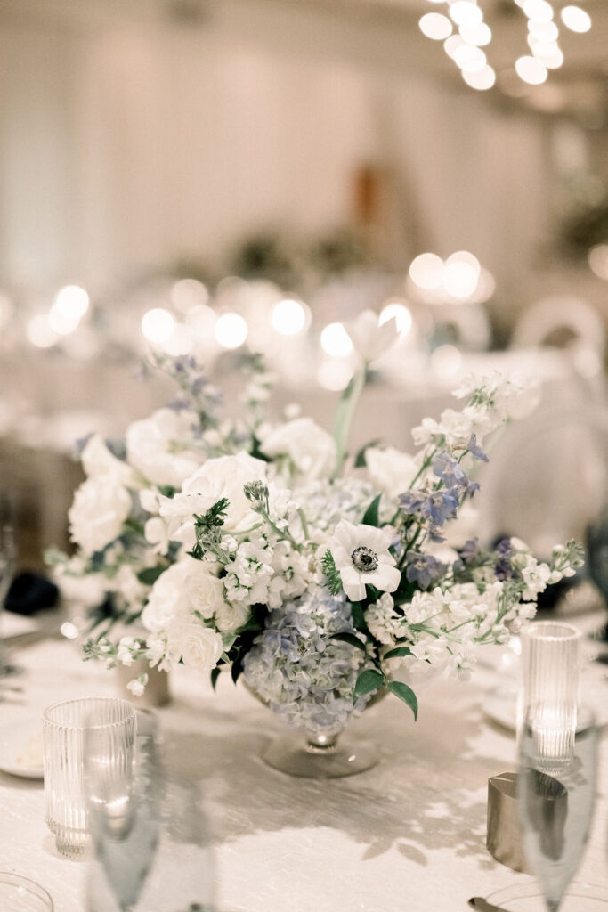 Low floral centerpiece of white and blue flowers for wedding reception.