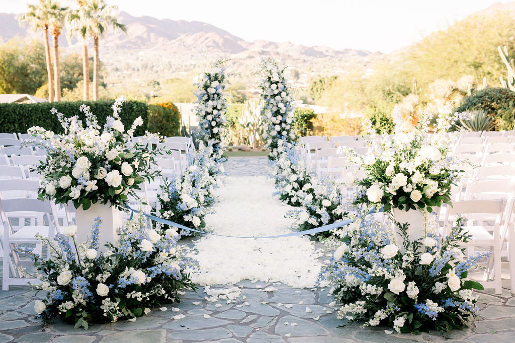 Wedding ceremony floral design with floral pillars and white rose petals down aisle and arrangements on aisle sides.
