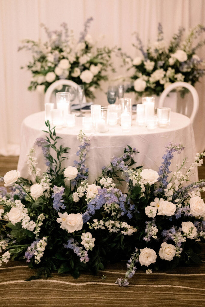 White and blue floral arrangements in front of sweetheart table with different height pillar candles.