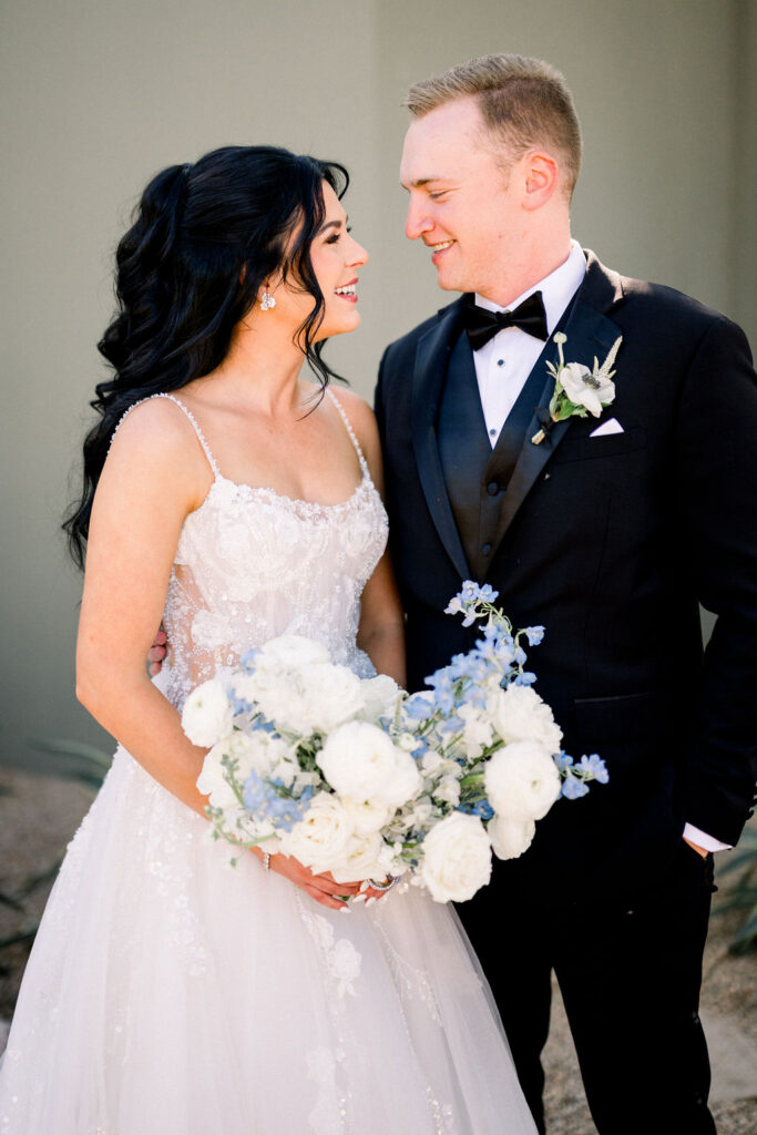 Bride and groom smiling at each other, bride holding bouquet.