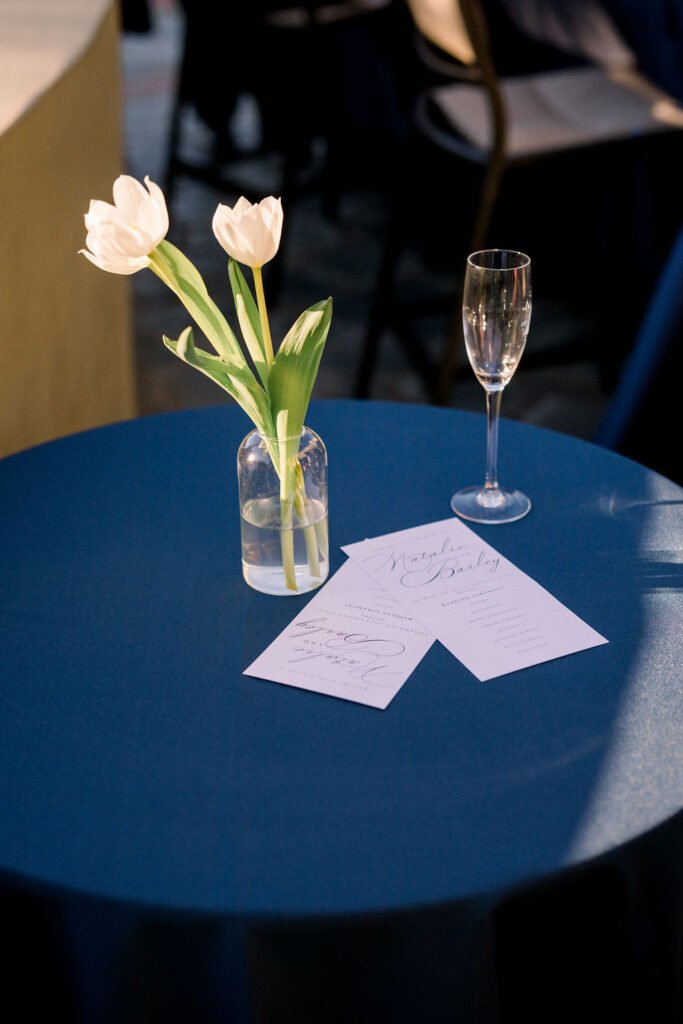 Elegant glass bud vase with white tulips on cocktail hour high table of navy linen.