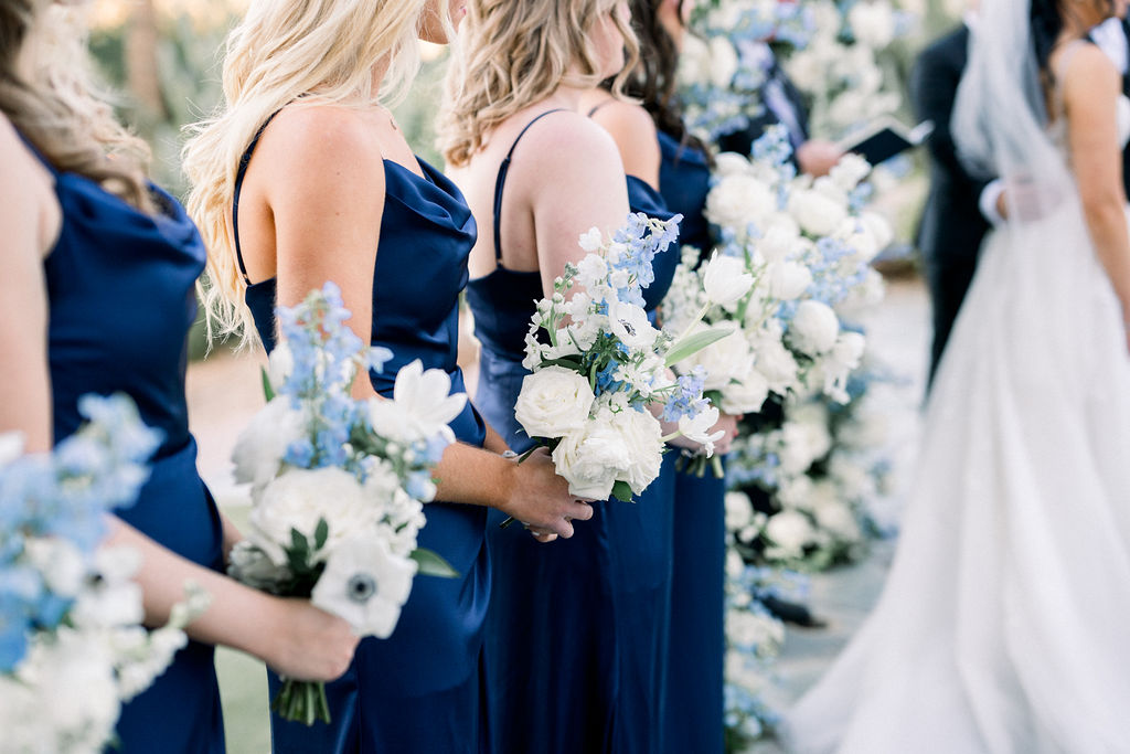 Bridesmaids in navy dresses holding white and blue floral bouquets.