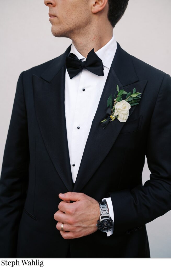 Groom in black suit with white flower boutonniere and greenery.