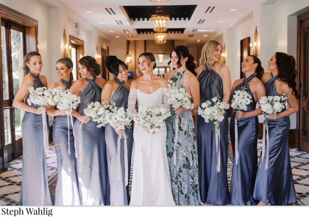 Bride standing in a line indoors with bridesmaids in shades of blue satin dresses.