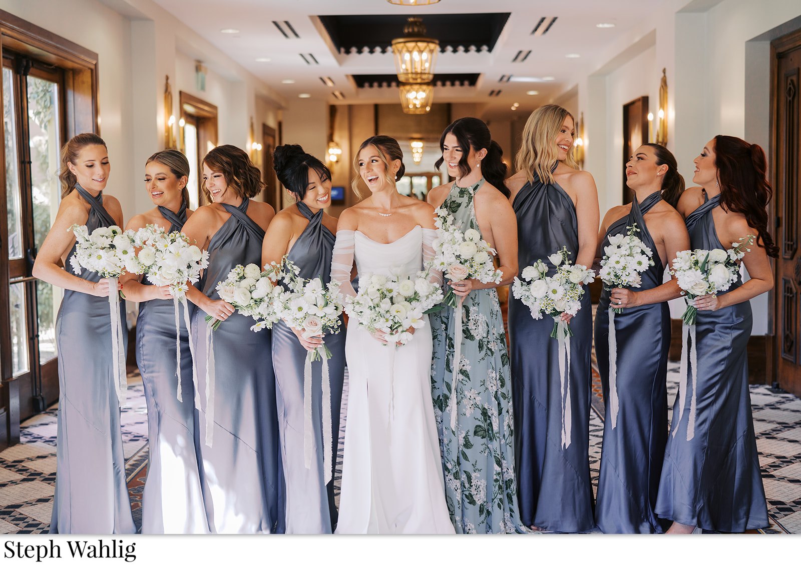 Bride standing in a line indoors with bridesmaids in shades of blue satin dresses.