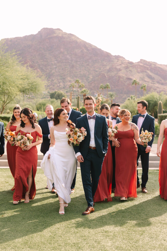 Bride and groom walking with wedding party with Camelback Mountain in background.