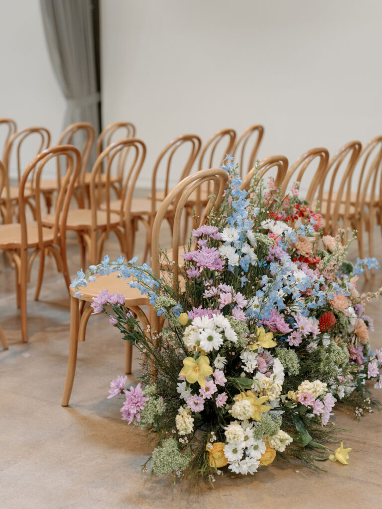 Back of wedding ceremony aisle ground floral in different shades of spring yellow, white, pink, blue and green colors.