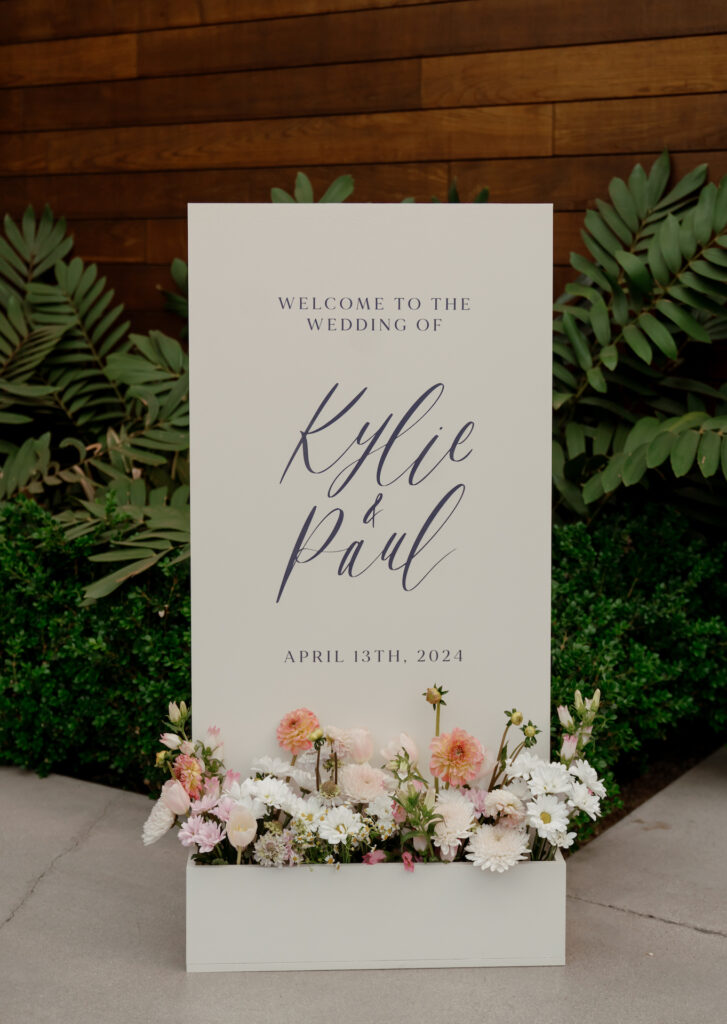 Custom welcome sign for wedding with flowers in box at bottom of sign.
