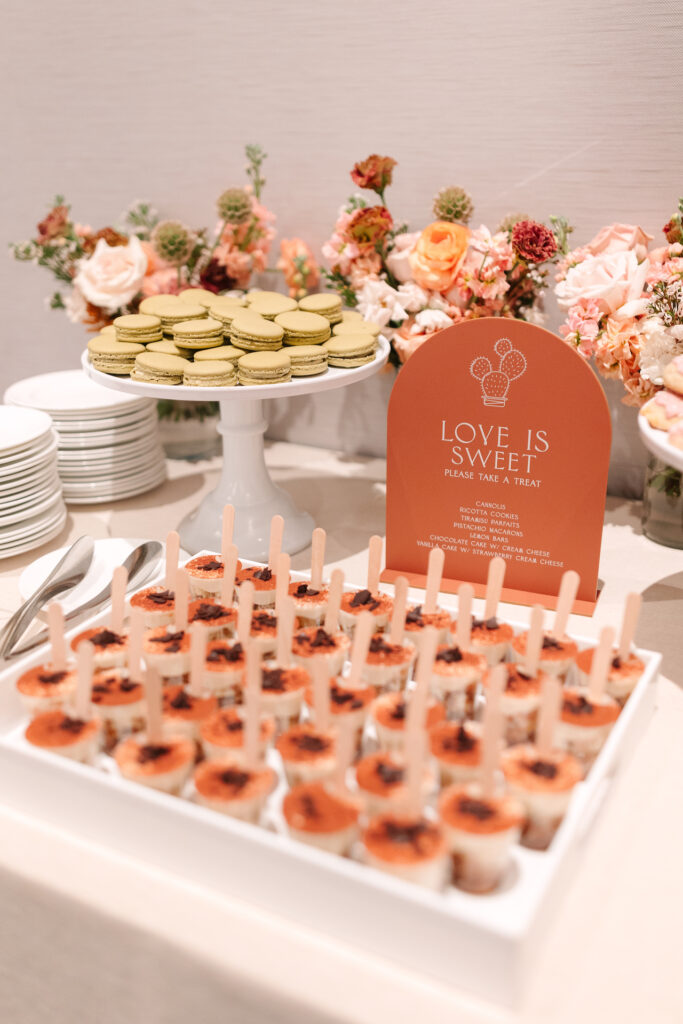 Wedding dessert table treats including macaroons with flowers in vases along the back of the wall.
