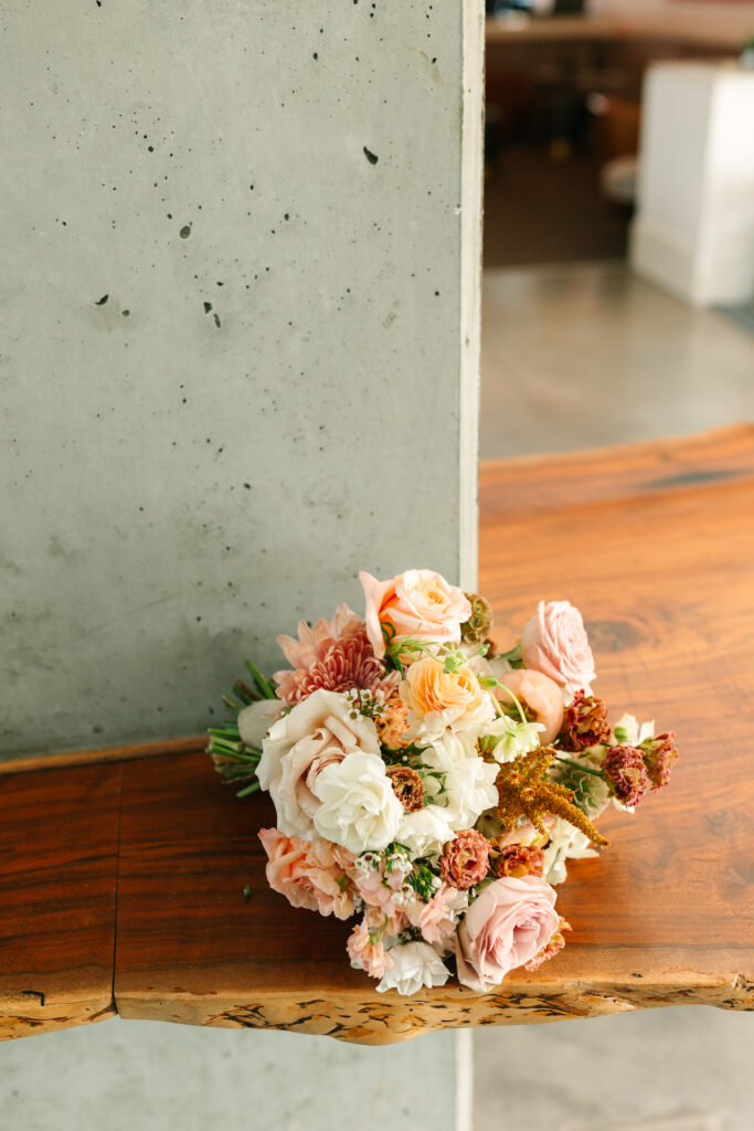 Bridal bouquet resting on wood slab counter and concrete wall.