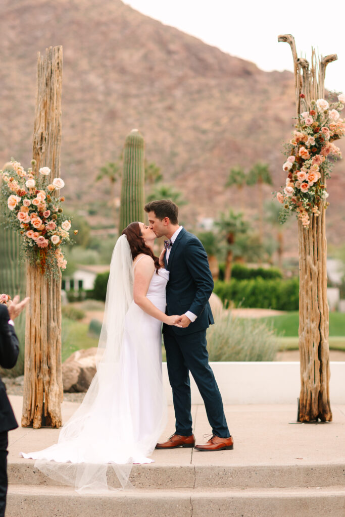 Bride and groom kissing between saguaro cactus ribs with floral attached in wedding ceremony altar space.