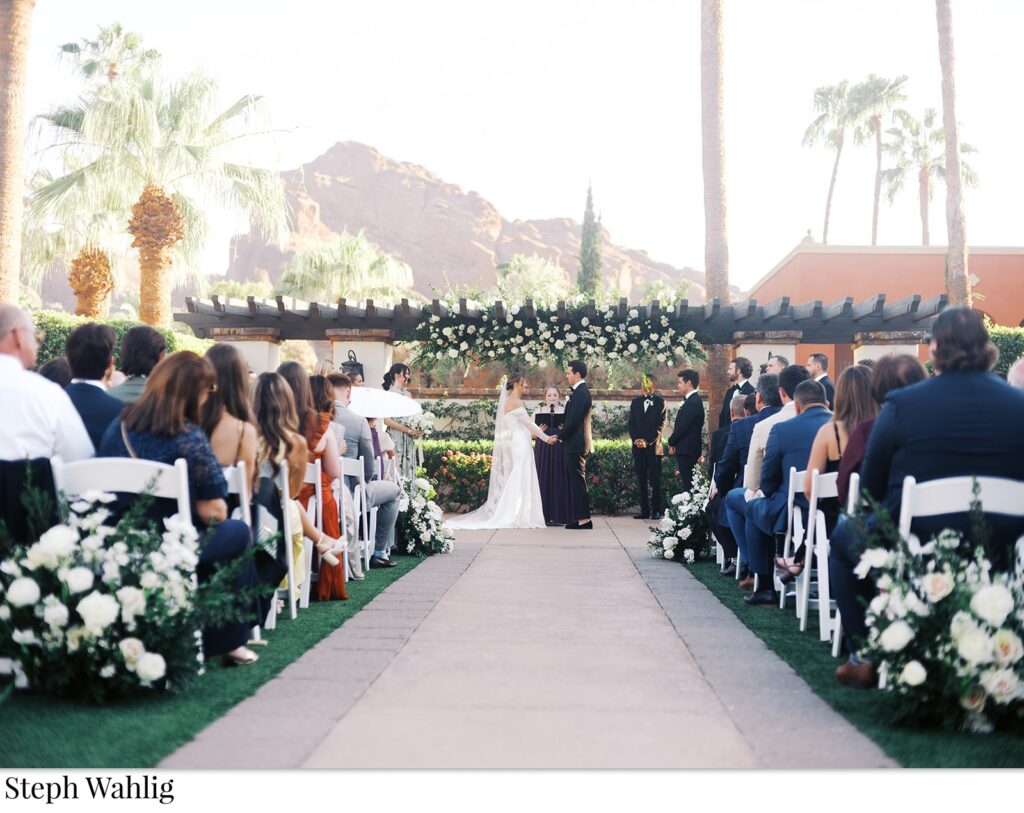 Bride and groom at wedding ceremony altar space at Omni Resort with floral installation on pergola above them.