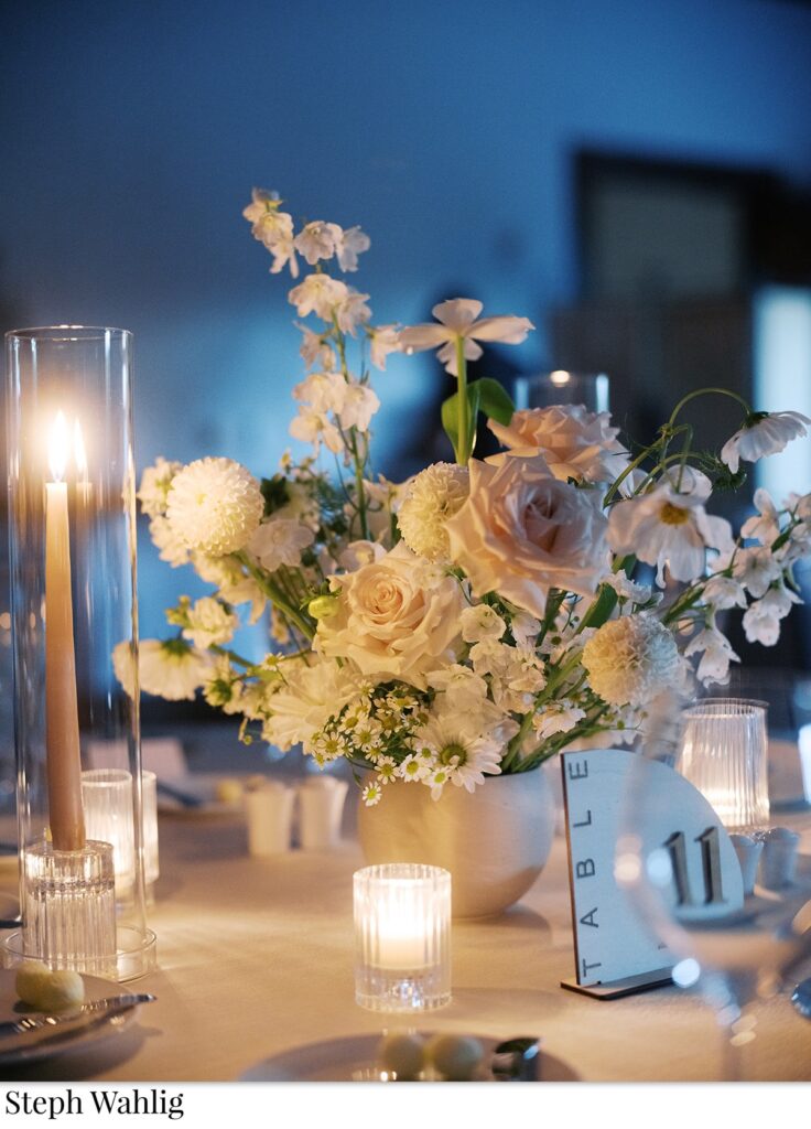 Wedding reception small floral centerpiece with votive candles and taper candles by it.