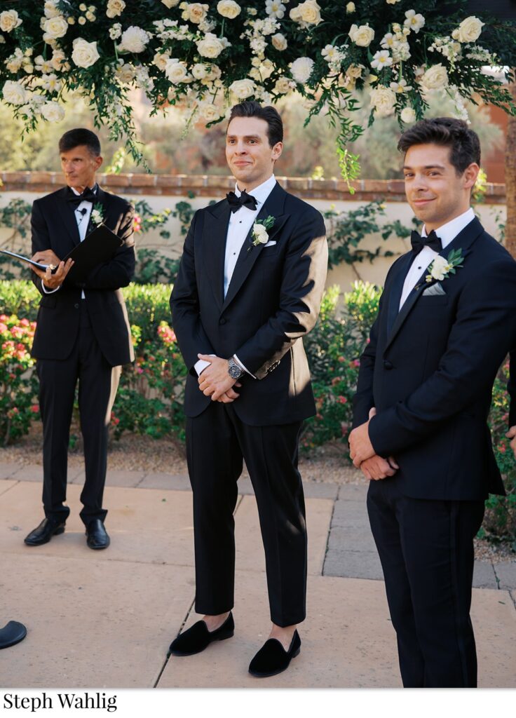 Groom standing in ceremony altar space with groomsmen, and officiant, smiling.