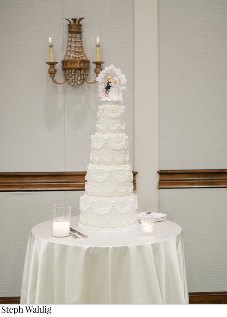 Tall four tiered white wedding cake with frosting detail and cake topper.