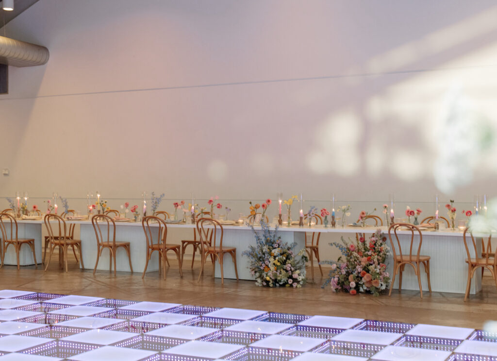 Long head table at wedding reception with ground floral arrangements in front of bride and groom spot.