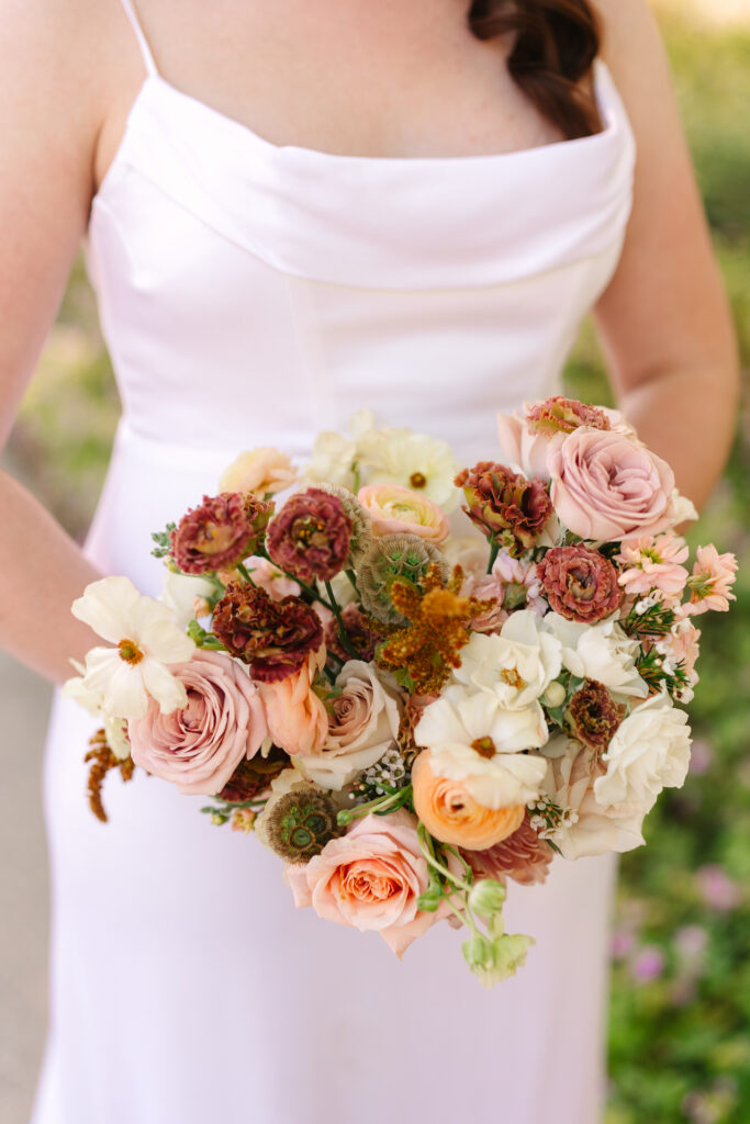 Bride holding bouquet of sunset colors flowers.