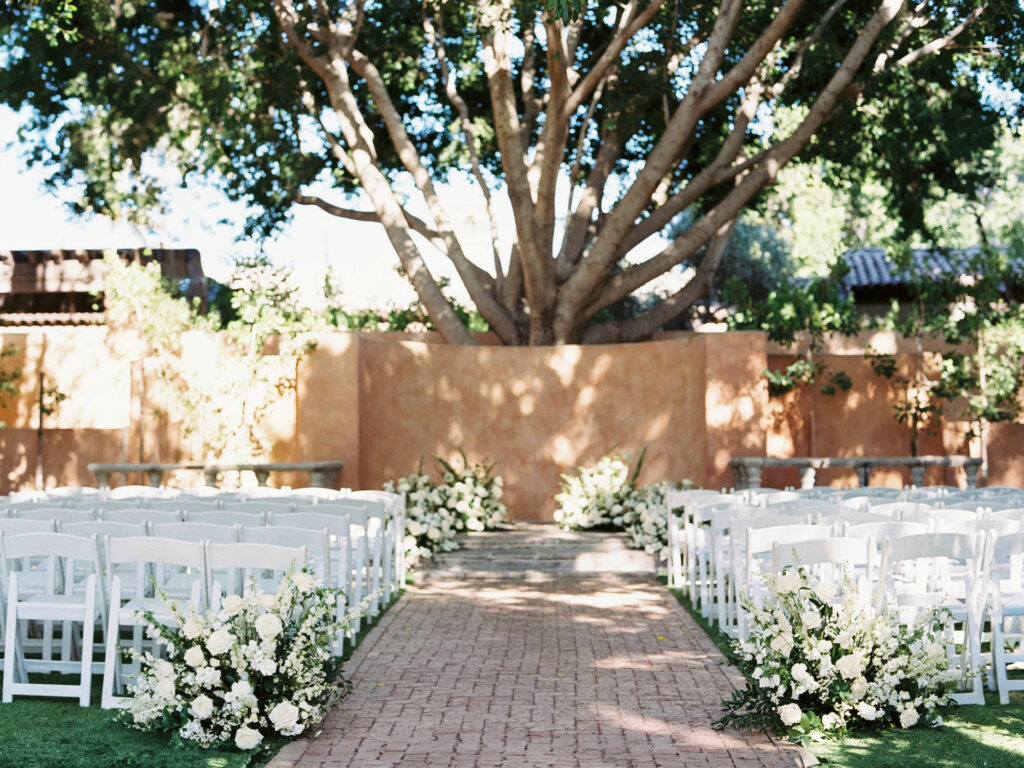 Wedding ceremony space at Royal Palms set with white chairs and floral designs of white flowers and greenery.
