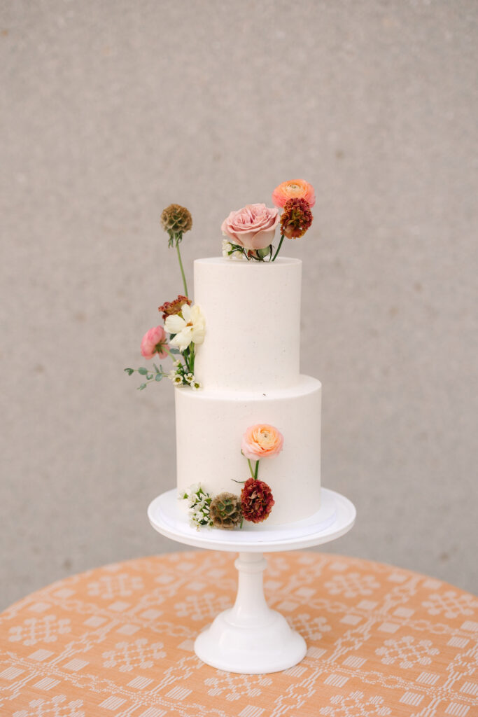 Two tiered smooth white wedding cake with sunset colors flowers placed on cake.
