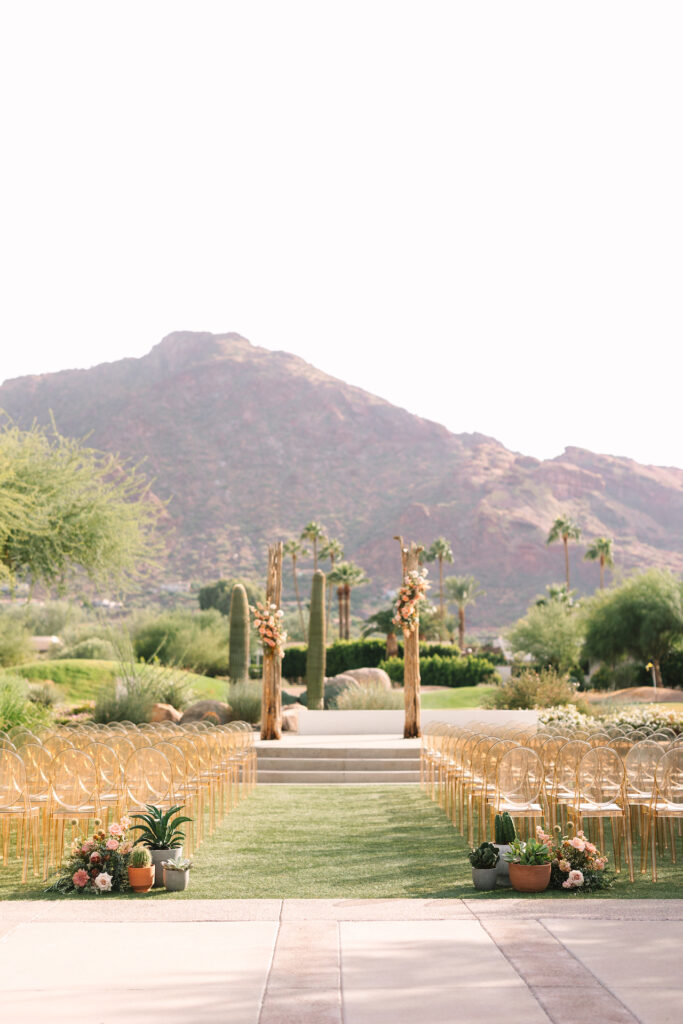 Wedding ceremony space at Mountain Shadows with gold acrylic guest chairs, saguaro cacti rib altar design and back of aisle cacti, succulent and flowers.