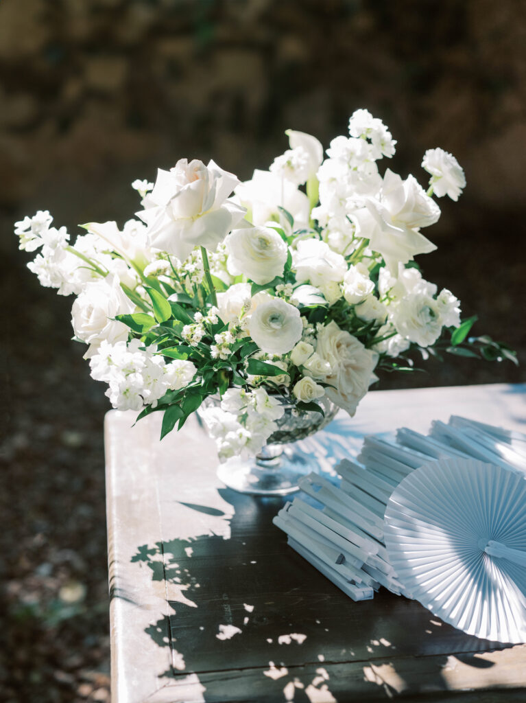Wedding floral design of white flowers and greenery in glass vase.