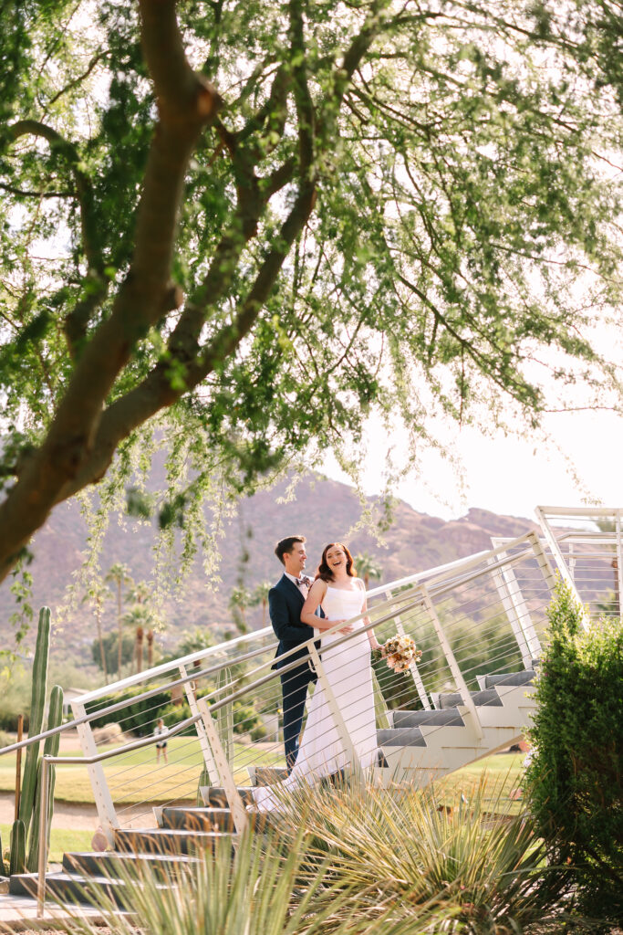 Bride and groom standing on stairs at Mountain Shadows, laughing.